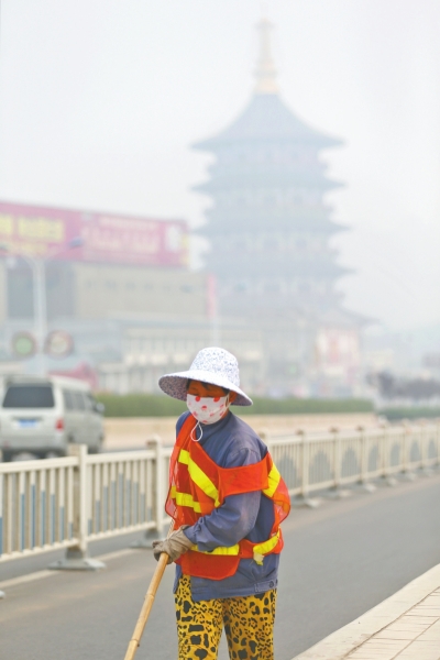 近日，在古都洛陽(yáng)，環(huán)衛(wèi)工人身后的“天堂”被霧霾籠罩著。