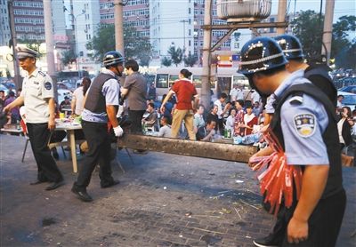 6月13日晚8點(diǎn)，朝陽路和青年路交叉口西側(cè)，一次聯(lián)合執(zhí)法行動中，輔警與協(xié)管抬走商戶的燒烤用具。新京報(bào)記者 尹亞飛 攝