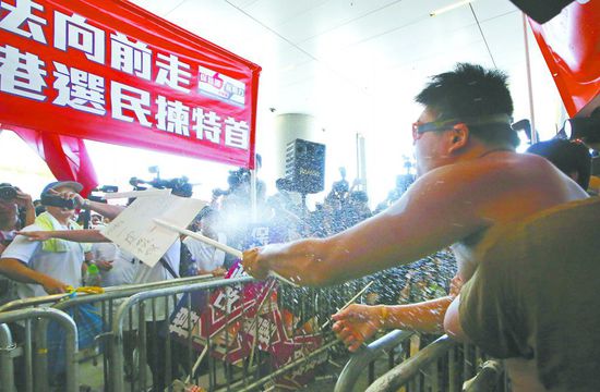 17日，在香港立法會(huì)外，一名反對政改的男子向支持派人群投擲標(biāo)牌。