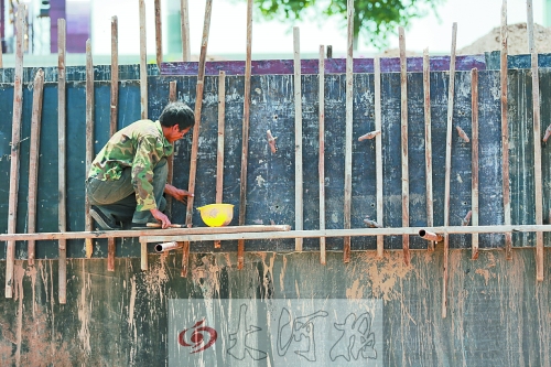 　　烈日下，狹窄的架子上，工人正用錘子固定樁基。