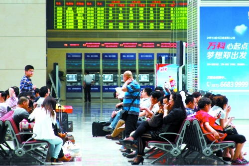 候車大廳溫度很高，一名乘客一手扇風(fēng)、一手擦汗