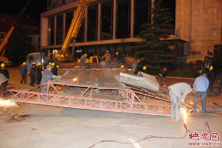 地面上的20多名工人對吊裝下的廣告牌進(jìn)行分割。