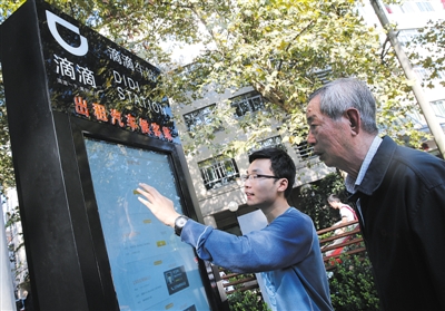 10月15日，滴滴工作人員（左）指導(dǎo)乘客使用“滴滴車站”的電子屏預(yù)約出租車。