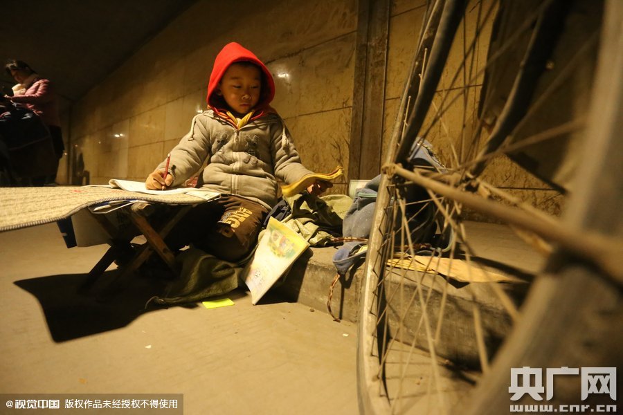 2015年11月8日晚，鄭州，7歲男孩涵洞橋下陪父母練攤，路邊燈下坐小馬扎上寫作業(yè)。