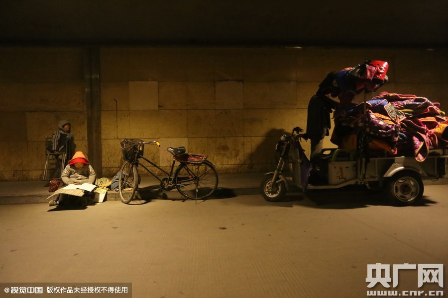 2015年11月8日晚，鄭州，7歲男孩涵洞橋下陪父母練攤，路邊燈下坐小馬扎上寫作業(yè)。