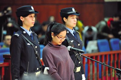 被告人盧梅低著頭，站在朝陽法院刑事審判庭的被告席上。