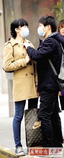 公交站臺上，一對年輕人戴著口罩，系緊衣領(lǐng)。